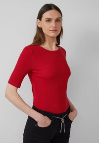 Rode geribbelde top met korte mouwen en een ronde hals. Gladde textuur met een aansluitend ontwerp. Draag met zwarte broek, handen in de zakken.