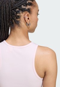 Svetlo ružová rebrovaná tielko s okrúhlym výstrihom, ktorý ukazuje hladkú textúru a široké ramenné otvory, doplnené striebornými kruhovými náušnicami.