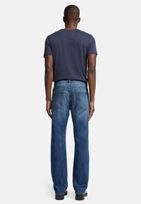 Granatowa bawełniana koszulka w połączeniu z prostymi dżinsami w kolorze niebieskim. Dżinsy mają pięć kieszeni i przetarcia. Czarne obuwie dopełnia strój.