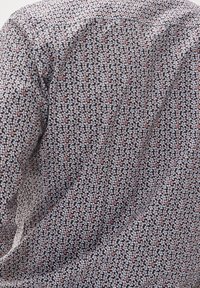 Camicia in cotone con sfondo blu navy, caratterizzata da un motivo ripetitivo di piccole foglie in blu pallido, bianco e rosa. Texture morbida, vestibilità slim.