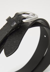 Ceinture en cuir noir avec un motif texturé, dotée d'une boucle en métal argenté. Le design comprend une boucle pour la sangle et plusieurs trous de réglage.