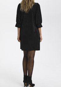 Svart randig kort klänning med puffärmar och strukturerad tyg. Kombinerad med svarta ankelskor och genomskinliga strumpbyxor. Enkel, modern siluett.