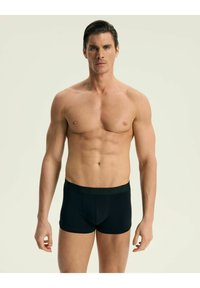 Czarne bokserki z miękkim pasem, o dopasowanym kroju, gładkiej fakturze i przedniej kieszeni zapewniającej wsparcie. Model ma muskularną sylwetkę.