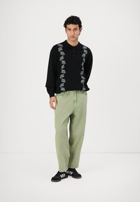 Black long-sleeve shirt with floral embroidery, buttoned collar; paired with light green wide-leg jeans and black athletic shoes.