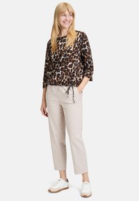Leopardenmuster-Bluse mit Dreiviertelärmeln und gerafftem Saum, kombiniert mit hellbeigen Leinenhosen und weißen Sneakern mit braunen Akzenten.