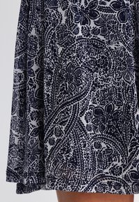 Laivastonsininen ja valkoinen kuvioitu hame, jossa on monimutkaisia kukka- ja paisley-kuvioita, valmistettu sileästä kankaasta, joka on virtaava ja kevyt.