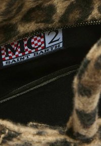 Detalle del interior de una bolsa de tela con estampado de leopardo, mostrando un bolsillo con cremallera y una etiqueta que dice "MC2 Saint Barth" con un patrón a cuadros rojos.