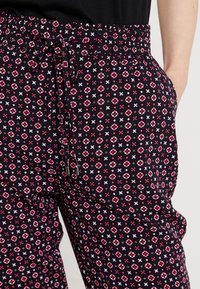 Czarne spodnie z kwiatowym i geometrycznym wzorem w kolorze różowym, czerwonym i białym. Posiadają elastyczny pas ze sznurkiem oraz kieszenie boczne.