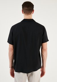 Lyhythihainen musta paita rentoa istuvuutta, jossa on tasainen kaulus ja sileä pinta. Minimalistinen muotoilu ilman näkyviä kuvioita tai yksityiskohtia.