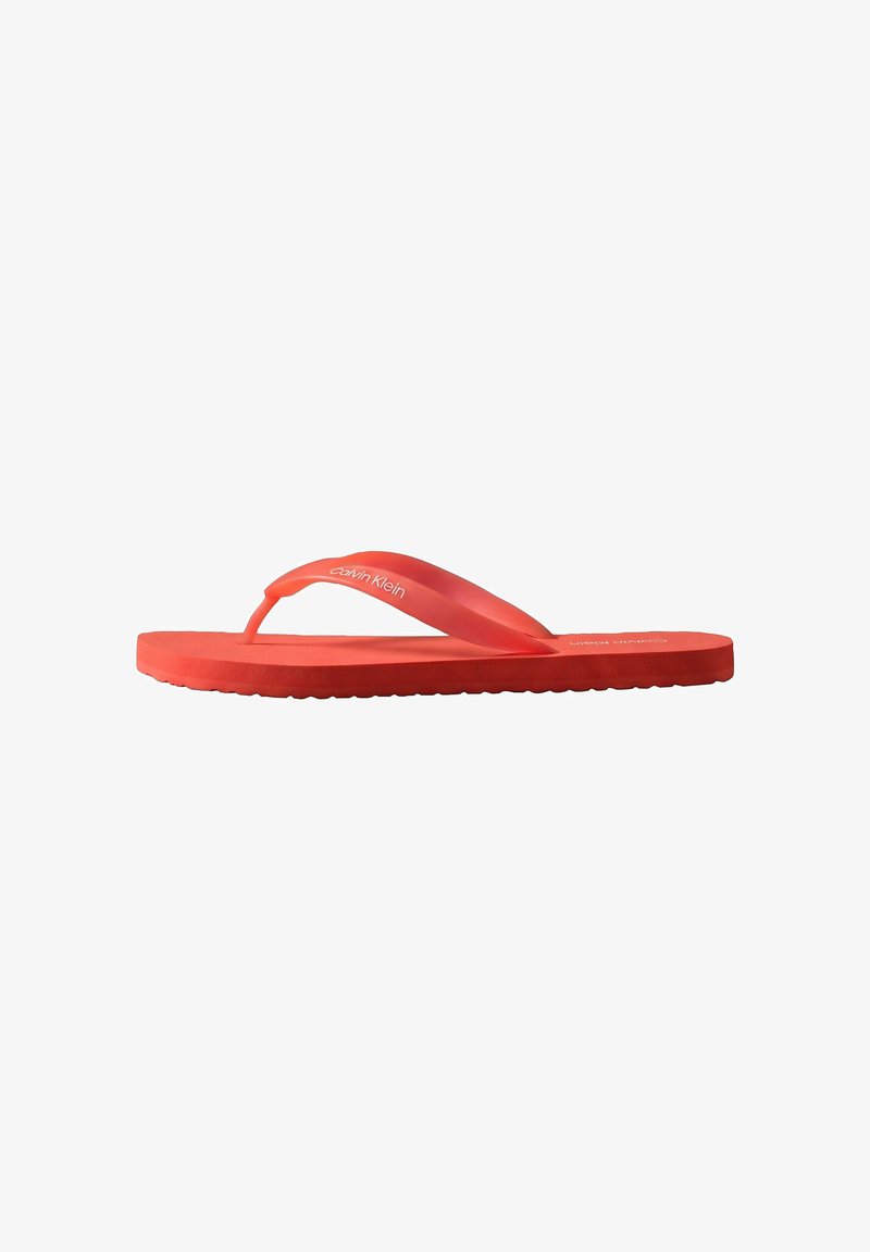 Tongs rouges Calvin Klein avec semelle en caoutchouc et bride entre les orteils, vue latérale sur fond blanc.