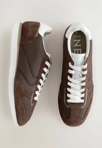 Zapatillas deportivas marrones hechas de ante y material sintético. Presentan cordones blancos, refuerzo en el talón y una textura contrastante en los laterales.