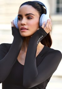 Melns garas piedurknes sporta tops ar gludu, gludu tekstūru, ar logo uz piedurknes, apvienots ar baltiem austiņām, kas uzliekamas uz auss.