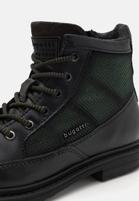 Juodi odiniai batai su žalia tekstūruota medžiaga, apvalūs raišteliai ir paminkštinta kraštinė. Turintys logotipo pleistrą ir kontrastingą siūlę.