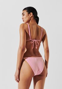 Juostuota bikini maudymosi kostiumėlį su rožinėmis ir baltomis vertikaliomis linijomis; reguliuojamos petnešėlės su rišimu gale. Medžiaga atrodo lygi ir prigludusi.