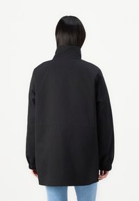Veste noire avec un col montant, des manches longues et des poignets élastiques. Réalisée en tissu lisse, elle présente une coupe décontractée avec un dos droit.