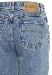 Blauwe denim jeans hebben een vervaagde afwerking, twee achterzakken en een tabblad van bruin leer met "BALL" op de tailleband. Standaard snit en stikseldetails.