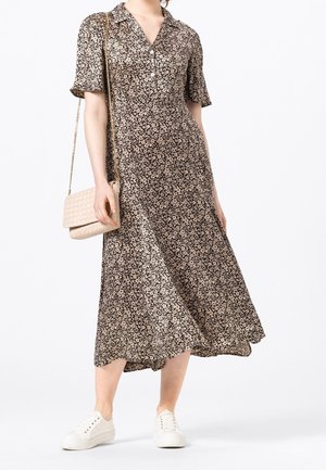 Femme portant une robe midi marron à fleurs avec manches courtes, des baskets blanches, et tenant un sac bandoulière beige avec une chaîne.