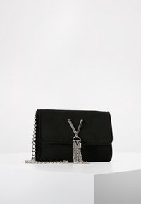 Black suede clutch with silver chain strap, silver "V" logo, and hanging silver chain tassel on white surface against a plain background.