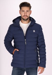 Marinblå puffjacka med zip-fram och huva. Har ett texturerat, kviltat mönster och logotyp på övre vänstra bröstet.