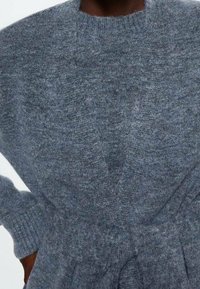 Szary sweter dziany z okrągłym dekoltem i długimi rękawami. Posiada teksturowane wykończenie oraz wiązanie w talii.