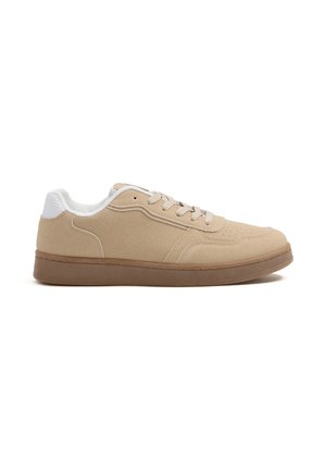 Zapatilla beige de ante tipo low-top con cuello acolchado blanco, suela de goma marrón claro y cordones beige, mostrada desde el lado interior sobre un fondo blanco.