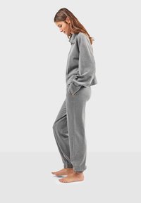 Šedá souprava mikiny a tepláků z měkké látky. Mikina má límec a kapsy, zatímco tepláky mají elastické manžety.