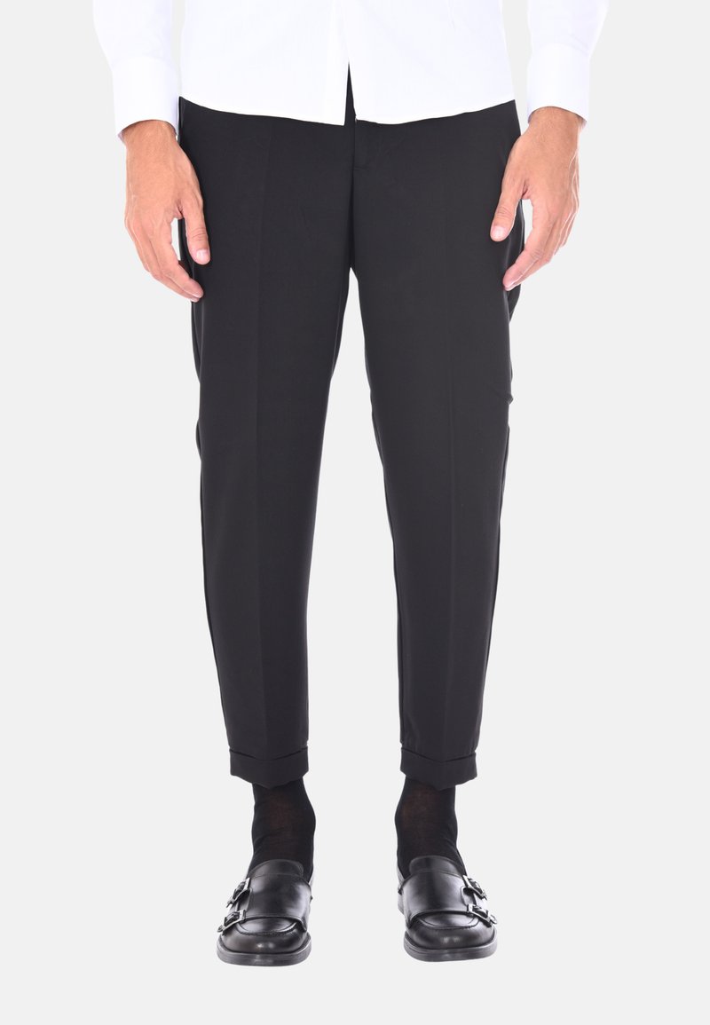 Pantaloni neri su misura con una texture liscia, caratterizzati da una vestibilità slim e orli risvoltati. Indossati con scarpe e calzini neri.