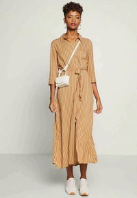 Rochie midi călduie cu dungi, cu mâneci lungi, legată la talie. Împreună cu o geantă mică albă tip crossbody și adidași albi.