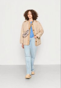 Jaqueta acolchoada bege com um colarinho castanho, t-shirt azul, jeans azul claro e tamancos beges. A segurar uma bolsa de padrão de leopardo.
