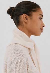 Sciarpa lavorata a maglia di colore crema drappeggiata attorno al collo, realizzata in tessuto morbido con una texture a coste. Caratterizzata da una vestibilità ampia e casual.