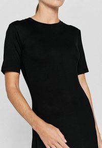 Sort kortærmet kjole lavet af glat stof, med en rund halsudskæring og tætsiddende silhuet, med subtile sømdetaljer synlige.