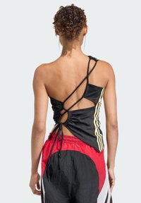 Czarny top bez rękawów z krzyżującym się z tyłu wzorem, ozdobiony żółtymi paskami i marszczeniami. Noszony z czerwono-czarnymi szortami.