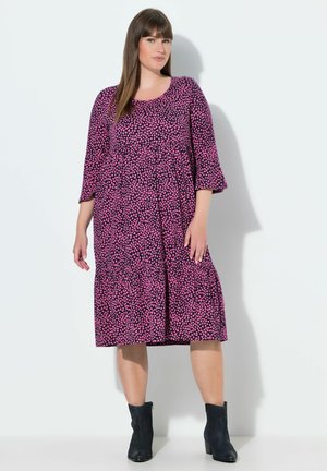 Fialové šaty s rozházeným vzorem růžových srdcí, kulatý výstřih, tříčtvrteční rukávy, vícedílný střih, kombinované s černými kotníkovými botami.