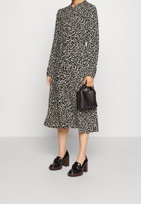 Woman wearing a long-sleeve, patterned midi dress, holding a small black handbag, and wearing black heeled loafers with wooden soles.