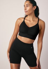 Zwarte sportbeha met ruchingdetails en verstelbare bandjes, gecombineerd met zwarte high-waisted fietsshorts met een gladde textuur.