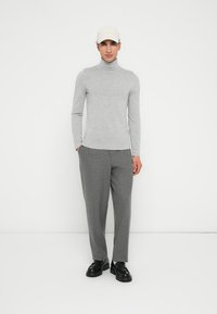 Ljust grått polotröja i kombination med löst sittande grå byxor och svarta skor. Modellen bär en ljusbeige basebollkeps.