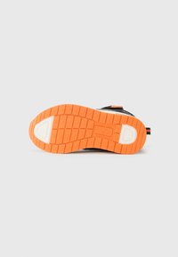 Sola de borracha laranja e branca de um sneaker preto, mostrando o padrão de pisada com grips quadrados e circulares sobre um fundo branco.