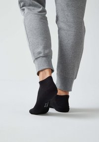 Calze nere a caviglia con un motivo di maglia testurizzata, indossate con pantaloni sportivi grigi, che mettono in evidenza il polsino a coste della calza e il materiale morbido.