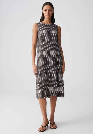 Donna snella che indossa un abito senza maniche, lungo fino al ginocchio, nero e bianco con fantasia, orlo arricciato e sandali neri con tacco.