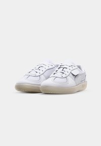 Chaussures de sport blanches avec une tige en cuir lisse, des accents en mesh, des lacets plats et une semelle en caoutchouc texturée. Design minimaliste sans motifs.