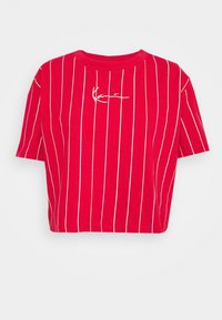 Punainen lyhythihainen lyhyt t-paita, jossa on valkoisia ja monivärisiä pystysuoria raitoja. Edessä on valkoinen allekirjoituslogo.