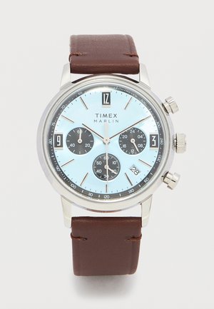 Montre-bracelet Timex Marlin avec cadran bleu clair, trois sous-cadrans noirs, boîtier argenté, bracelet en cuir marron, et guichet de date à 16 heures.