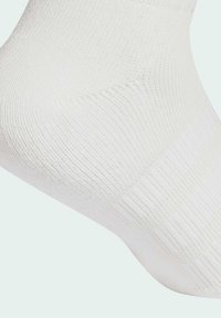 Biele členkové ponožky vyrobené z textúrovanej látky, s horizontálnym rebrovaním a zosilnenou pätou pre vyššiu odolnosť.