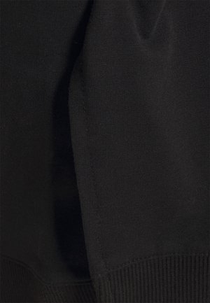 Gros plan sur un tissu noir montrant une bordure côtelée et une texture tricotée lisse sur la manche d'un vêtement.