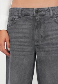 Gray denim jeans with a slight wash effect, featuring a button closure, front pockets, and a straight-leg cut. Textured fabric with subtle lines.