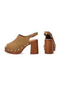 Tan suède open-toe klompen met een houten blokhak, voorzien van goudkleurige studs aan de voorkant en een verstelbare enkelband.