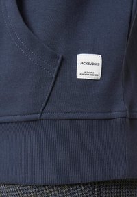Sweatshirt bleu marine avec un ourlet côtelé texturé. Comprend une petite étiquette tissée blanche avec "JACK & JONES" et "AUTHENTIC JEANSWEAR SINCE 1990."