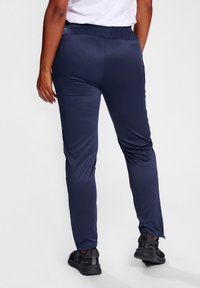 Mariene atletische broek met een gladde, glanzende textuur, voorzien van een elastische tailleband en taps toelopende benen. Draag met zwart-witte sneakers.