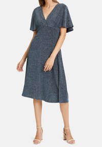 Třpytivé modré šaty s výstřihem do V, volánovými rukávy a sukní sahající ke kolenům. Látka má texturovaný, lesklý povrch.