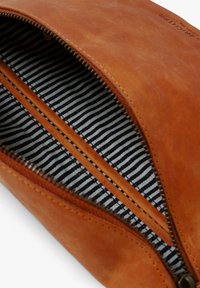 Braune Leder-Reißverschlusstasche mit gestreiftem Stofffutter. Verfügt über eine einzelne Innentasche und eine glatte, matte Außenoberfläche.